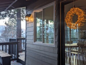 A wooden deck with a bench, a window with a wreath, and a table with chairs. - Nordic Holiday Home - Hot Tub, Sledding Hill, Included EV/Tesla Charger, Pets ok (Running Springs)