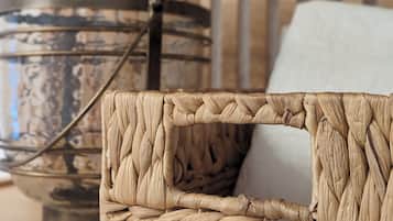 A woven basket with a handle, a decorative metal container, and a cushion on a wooden surface.