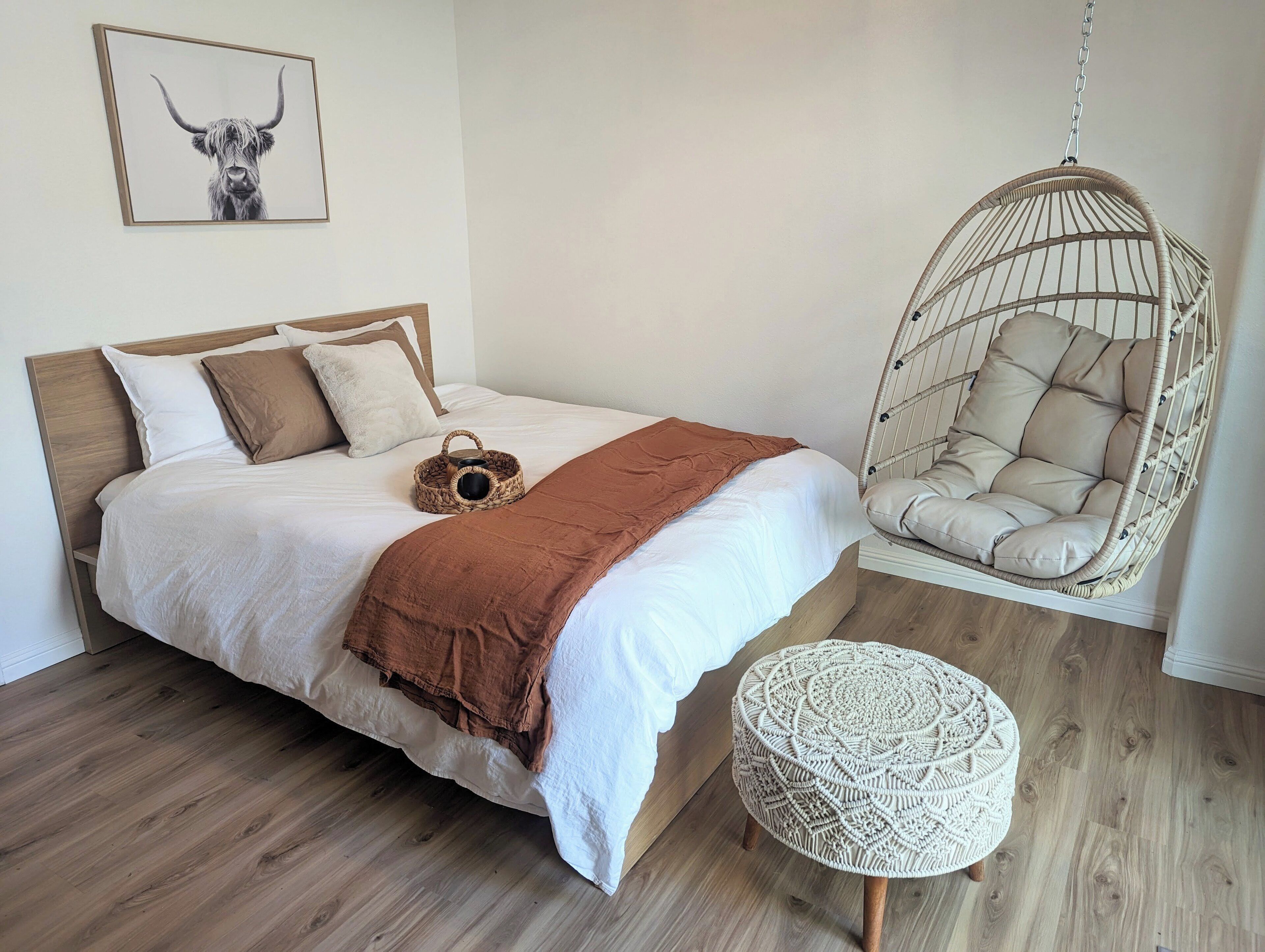 A bedroom with a bed, a hanging chair, and a round ottoman.