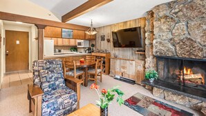 A cozy living room with a fireplace, wooden furniture, and a stone accent wall. - Lichenhearth 16 (Snowmass Village)