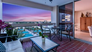A balcony with a view of a cityscape at sunset, a ceiling fan, and a table with chairs. - Palm Bay Club 8th Floor On Complex Private Beach (Siesta Key)