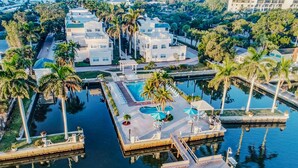 An aerial view of a resort with multiple buildings, a central pool area, and surrounding palm trees. - Palm Bay Club 8th Floor On Complex Private Beach (Siesta Key)