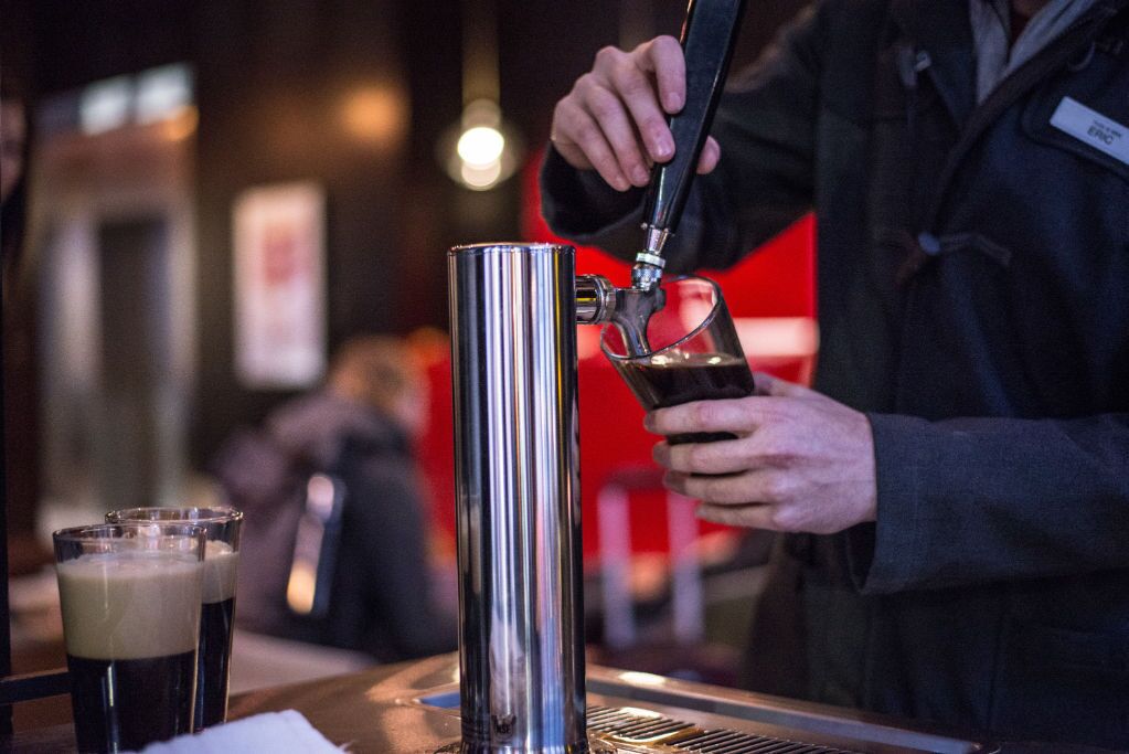 A bartender pouring a drink from a tap into a glass.