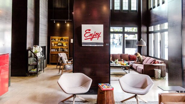 Un vestíbulo amplio con muebles modernos, un cartel que dice 'Enjoy' y una estantería con diversos objetos.
