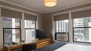 Een hotelkamer met een bed, een bureau met een televisie, en grote ramen met uitzicht op de stad.