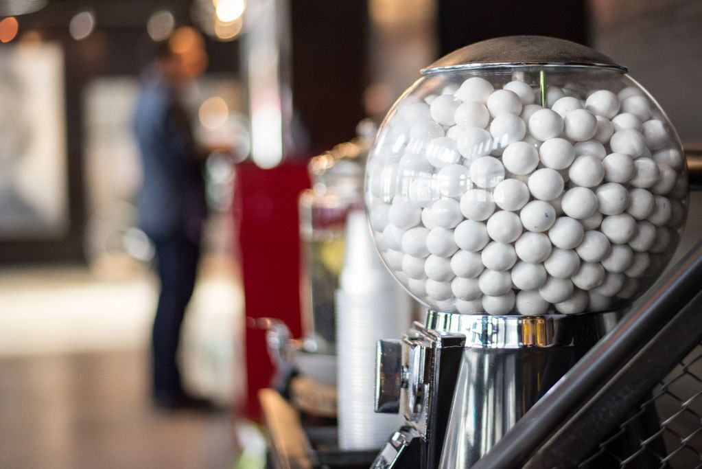 A clear glass gumball machine filled with white gumballs, mounted on a metallic stand.