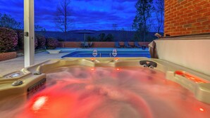 A hot tub with two faucets and a control panel, surrounded by a brick wall and a glass door leading to a patio area with outdoor seating and a pool. - Chattanooga Valley Paradise | Pickleball | Pool (flintstone)