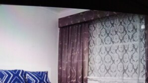 Un lit recouvert d’une couvre-lit à motifs, un plancher en bois et une fenêtre ornée de rideaux à motifs.