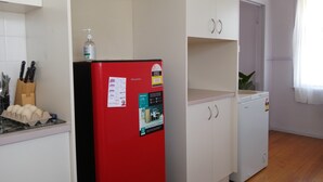Une cuisine de taille réduite avec un réfrigérateur rouge, des placards blancs et un petit plan de travail.