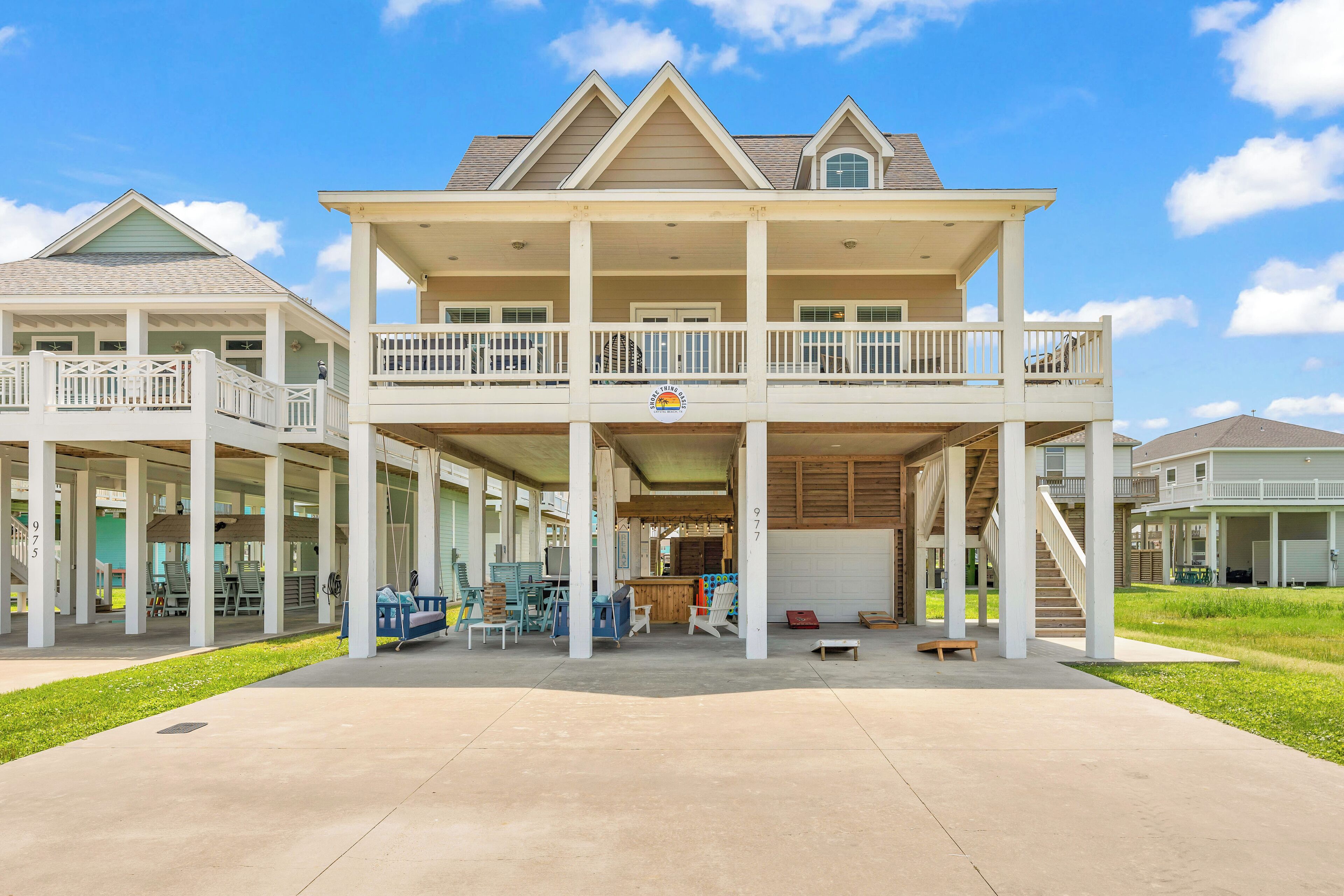 A two-story beachfront house with a covered porch, multiple balconies, and a bar area.