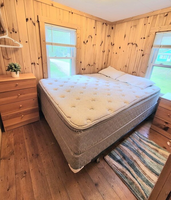 Een slaapkamer met een bed, houten wanden, een dressoir en een raam.