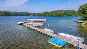 A dock with boats and a covered area, surrounded by a lake and forest.