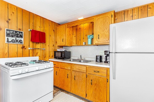 A compact kitchen with wooden cabinets, a white stove, a microwave, and a refrigerator.