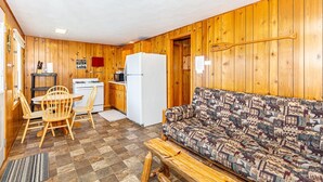 Ein gemütliches Blockhaus-Interieur mit Holzausstattung, einer Essecke mit Tisch und Stühlen, einer Couch, einem Kühlschrank und einer Mikrowelle.