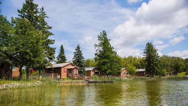 A lakeside cabin area with wooden cabins, a dock, and surrounding trees.