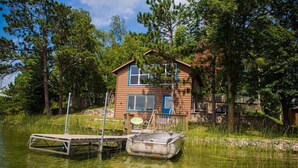 A cabin by a lake with a dock and a boat.