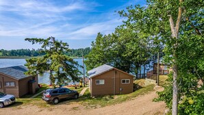 A lakeside cabin area with two cabins, a car, and a dock with boats.