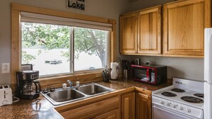A kitchen with wooden cabinets, a double sink, a microwave, a stove, and a coffee maker.