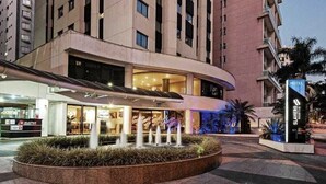 A hotel entrance with a modern design, a landscaped area with a water feature, and a visible MultiPark sign. - Flat com Cozinha Completa em Hotel Slaviero em Moema (Indianópolis São Paulo)