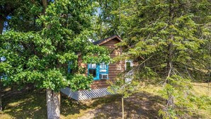 A log cabin with a white picket fence, surrounded by dense trees. - Cabin #7 - Gone Fishing (Lake Emma Township)