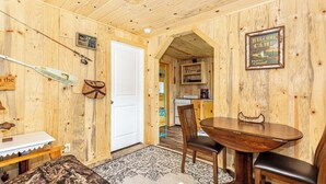 A wooden cabin interior with a dining table, chairs, a kitchen area, and a door leading to another room. - Cabin #7 - Gone Fishing (Lake Emma Township)
