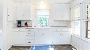 Una cocina con armarios blancos, una cafetera y un ventanal con persianas.