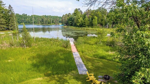 Una terraza de madera que da a un lago, con sillas y un pozo para fuego.
