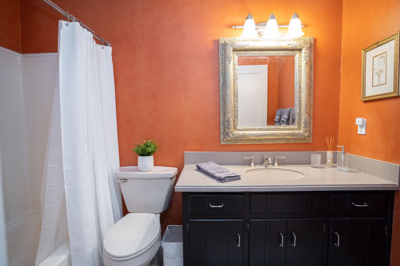 A bathroom with an orange wall, a white toilet, a black vanity with a mirror, and a shower curtain.