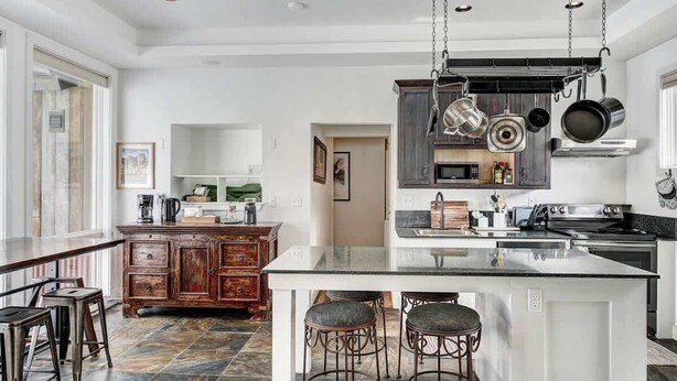 A modern kitchen with a central island, dark wooden cabinets, and hanging pots. - Aspen Grove Cabin w/Hot Tub (Fairplay)