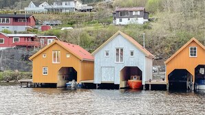 Trois bâtiments en bois, dotés de toits à pignons et construits sur pilotis au-dessus de l’eau, sont entourés de maisons et de collines.