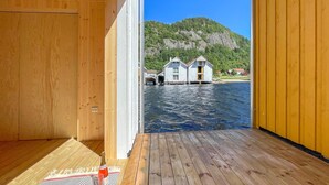 Une terrasse en bois avec une bouteille de champagne et des verres, donnant sur une étendue d’eau, avec des maisons et une montagne en arrière-plan.