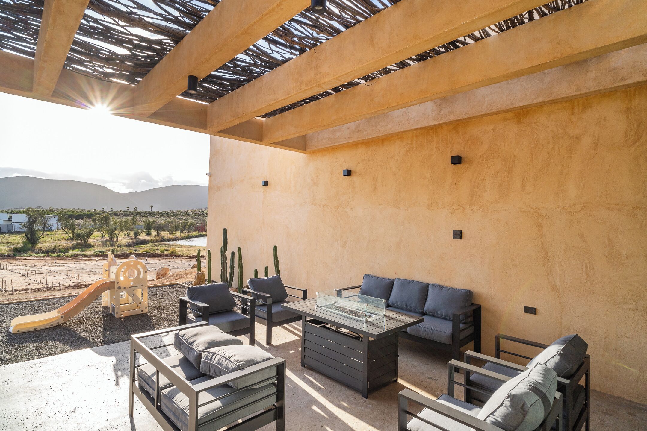 An outdoor patio area with a wooden pergola, seating arrangements, and a children's play structure.
