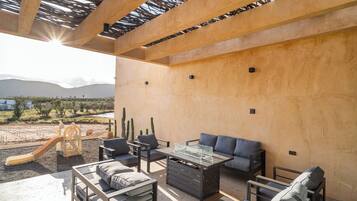 An outdoor patio area with a wooden pergola, seating arrangements, and a children's play structure.