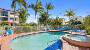 Una piscina con borde de azulejos, rodeada por una cerca blanca y palmeras al fondo.