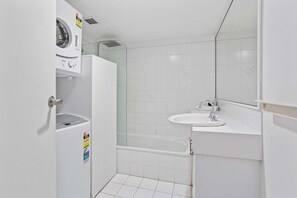 A compact bathroom with a washing machine, a glass-enclosed shower, and a sink. - Key Largo - Hosted by Burleigh Letting  (Burleigh Heads)