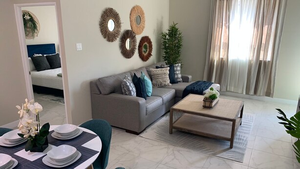 A modern living room with a grey sofa, a coffee table, and a dining area with a white table and chairs.