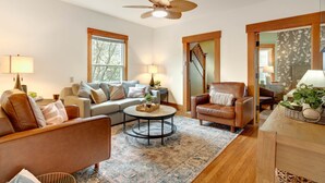 A living room with a sofa, armchair, coffee table, and a ceiling fan. - NEW Luxe on Front Downtown (Traverse City)
