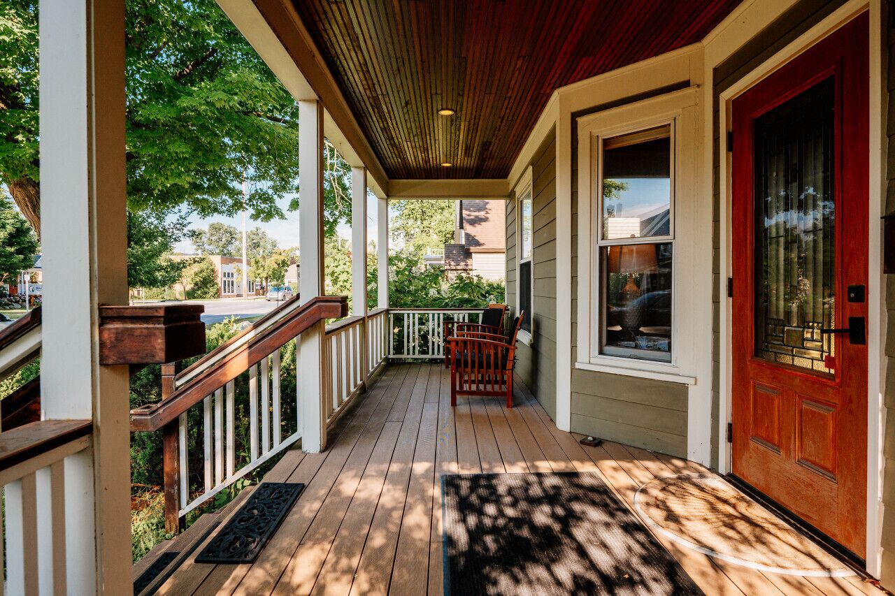 Une véranda en bois avec une porte rouge, des balustrades blanches et un banc.