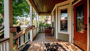 Une véranda en bois avec une porte rouge, des balustrades blanches et un banc.