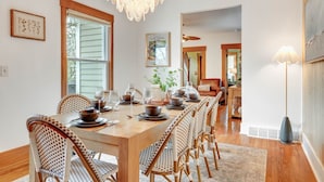 A dining room with a long wooden table set for six, surrounded by wicker chairs. - NEW Luxe on Front Downtown (Traverse City)