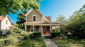 A two-story house with a front porch, a small front yard, and a clear blue sky. - NEW Luxe on Front Downtown (Traverse City)
