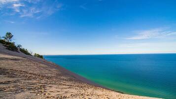 Une plage à l’eau d’un bleu limpide, avec un rivage sablonneux et une végétation clairsemée.