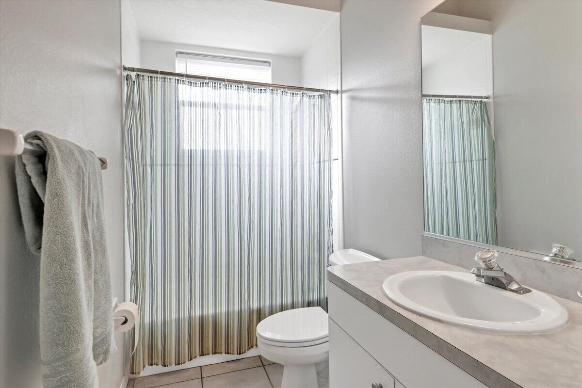 Un bagno con tenda doccia, water, lavandino e specchio.