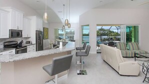 A modern kitchen with white cabinets, stainless steel appliances, and a central island with bar stools. - Seaclusion - stunning bayfront home with pool (Englewood)