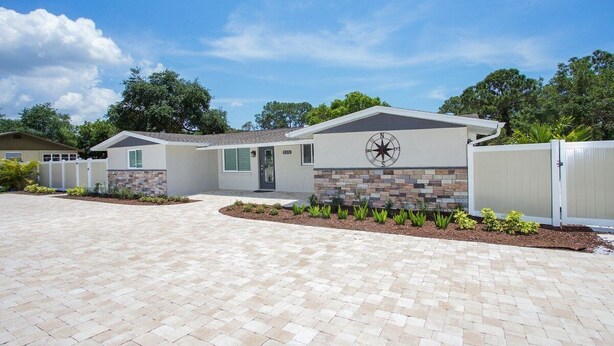 A modern single-story house with a paved driveway, a compass design on the wall, and a fenced yard. - Tropical Waterfront Oasis - Super Cute Home with your own Fishing Dock (Englewood)