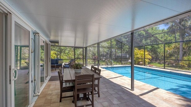 Un porche cubierto con piscina, mesa y sillas de madera.