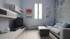 Ein modernes Wohnzimmer mit Flachbildfernseher, grauem Sofa, weißem Hocker und Heizkörper.