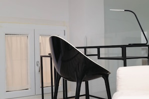 A room with a white chair, a black chair, a black metal desk, and a white door with a window.