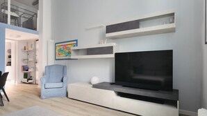Ein modernes Wohnzimmer mit Flachbildfernseher, Einbauschränken, einem hellblauen Sessel und einer Treppe, die zu einer oberen Ebene führt.