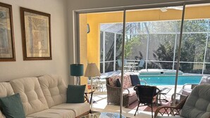 A living room with a beige sofa, wicker chairs, a glass coffee table, and a view of a swimming pool through large windows. - Parrot's Paradise - spacious walk to beach pool home with privacy (Englewood)